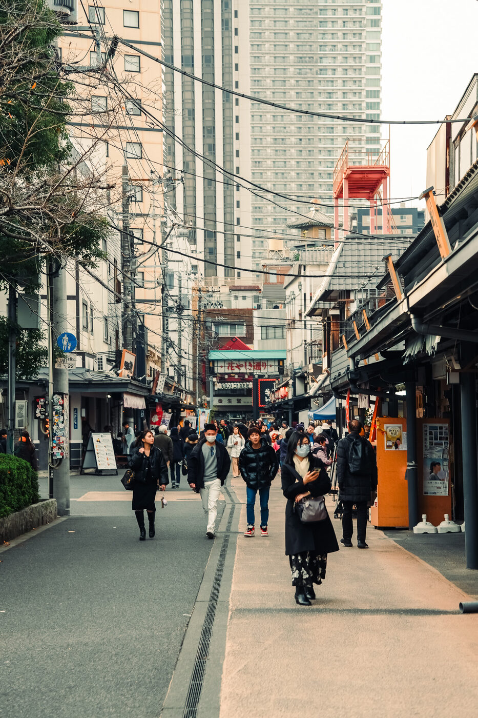 A shopping street in Asakusa, Tokyo — people walking between old shopfronts, towers rising behind